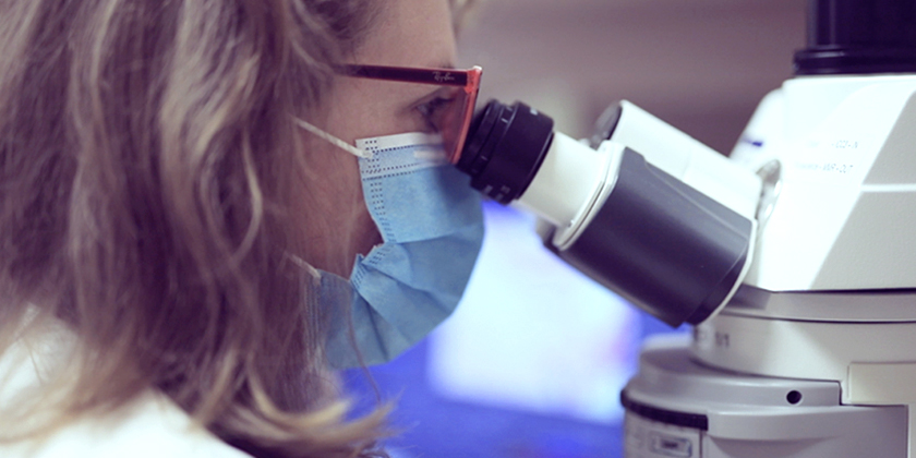 Vue latérale d'un chercheur en blouse et masque regardant à travers un microscope